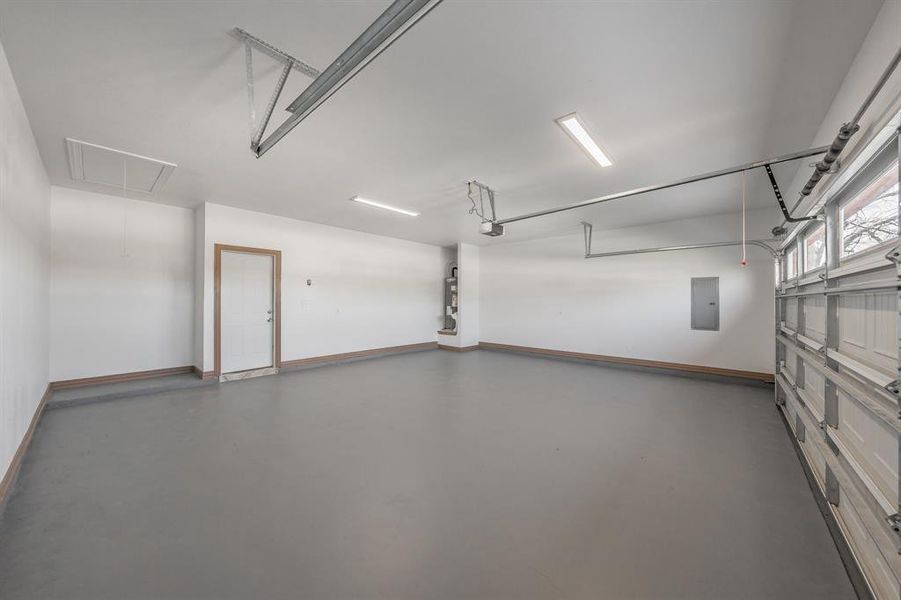 Garage featuring baseboards, electric panel, and a garage door opener