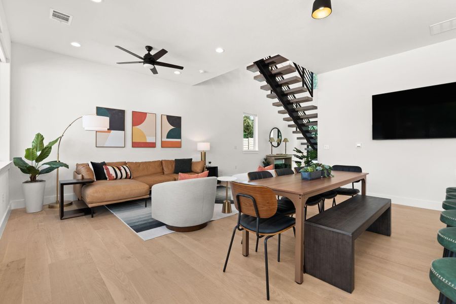 This modern, open-concept living and dining area features a sleek staircase, hardwood floors, and ample natural light. creating a welcoming atmosphere.