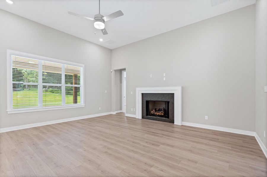 Spacious living area featuring light wood-finish flooring, a contemporary ceiling fan, recessed lighting, and a fireplace with a dark surround and white mantel Spacious living area featuring light wood-finish flooring, a contemporary ceiling fan, recessed lighting, and a fireplace with a dark surround and white mantel