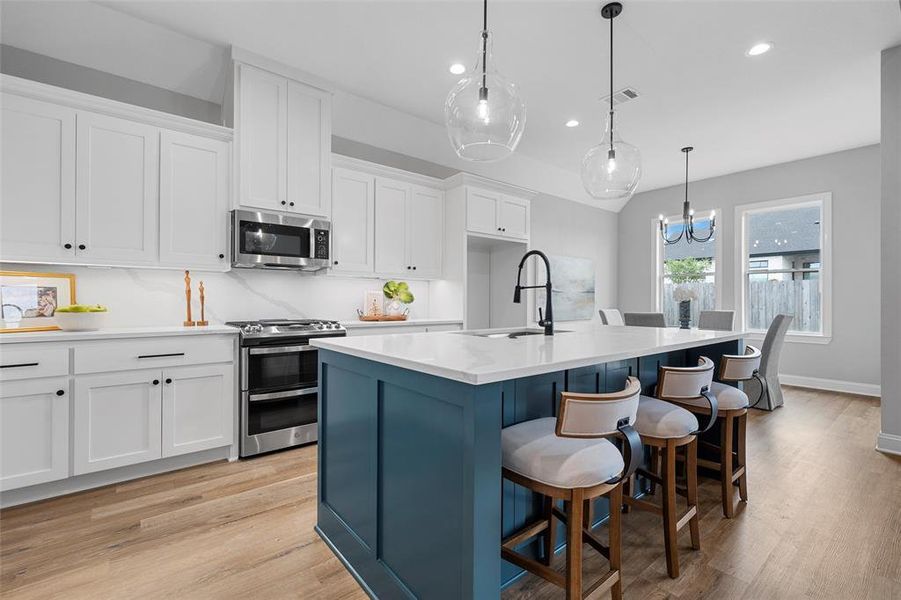 Kitchen featuring white cabinets, stainless steel appliances, light wood-style floors, decorative light fixtures, and recessed lighting Kitchen featuring white cabinets, stainless steel appliances, light wood-style floors, decorative light fixtures, and recessed lighting