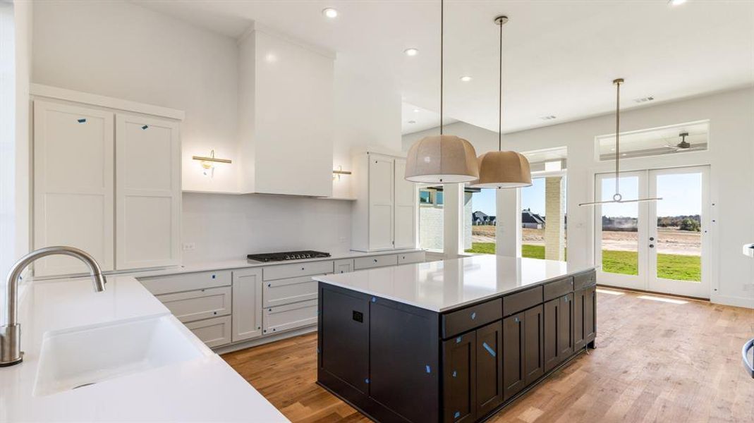 Kitchen with white cabinetry, sink, hanging light fixtures, stainless steel gas cooktop, and light wood-type flooring