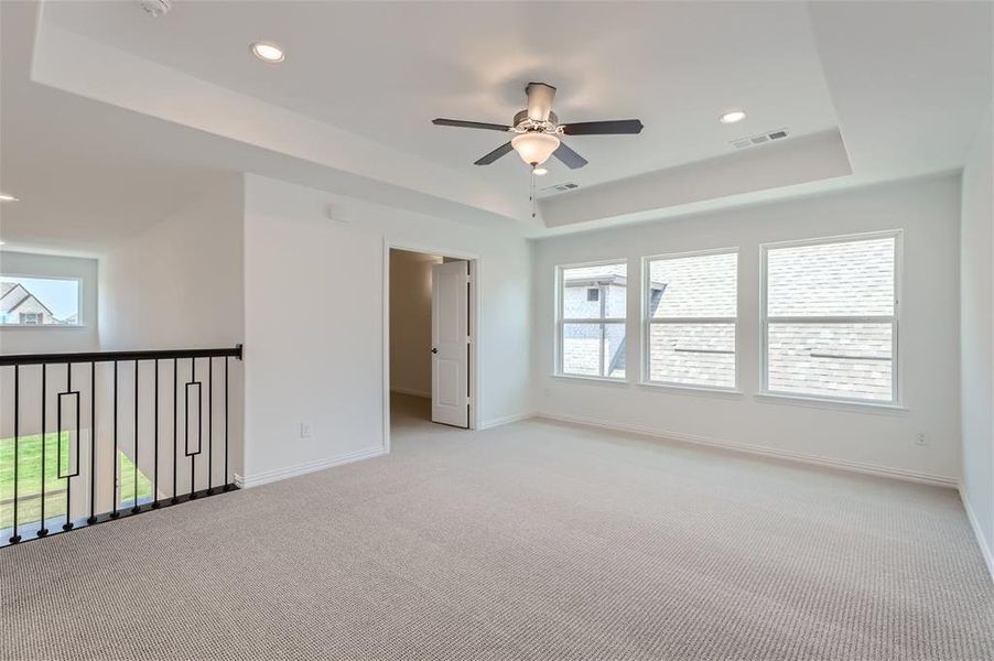 Carpeted spare room featuring a tray ceiling and ceiling fan