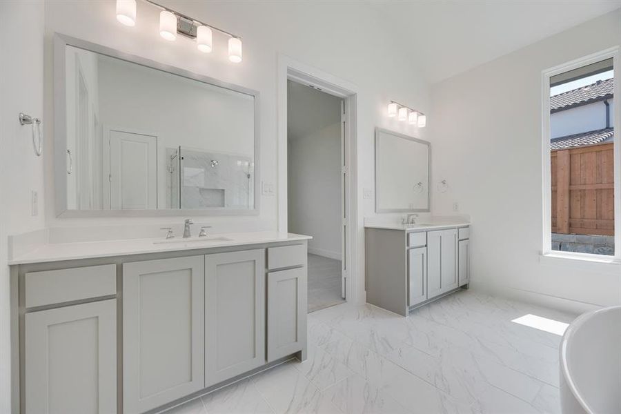 Bathroom with a marble finish shower, two vanities, a freestanding tub, vaulted ceiling, and light marble finish flooring