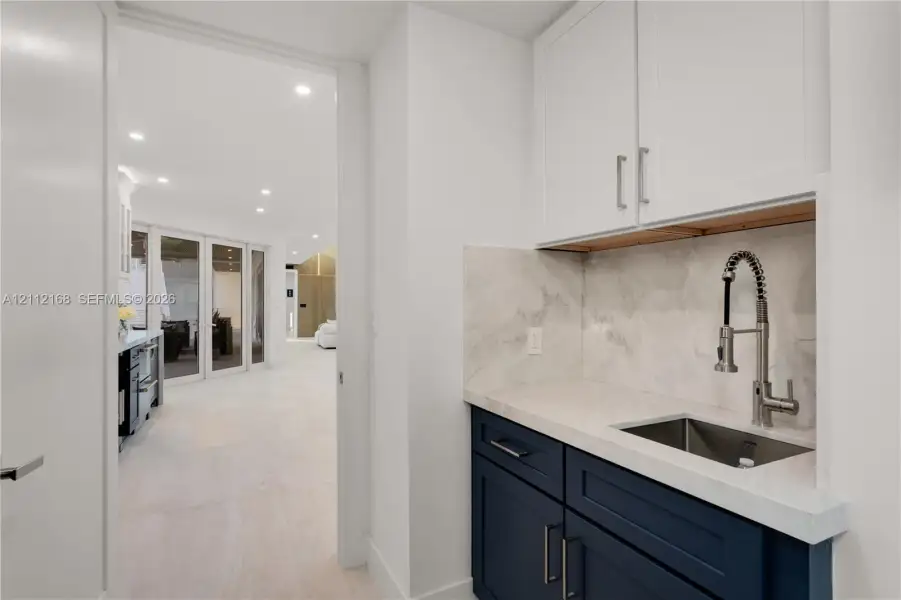 Wet bar featuring dark blue cabinetry, stone-finish countertop, coordinating backsplash, undermount stainless steel sink, and a gooseneck faucet Wet bar featuring dark blue cabinetry, stone-finish countertop, coordinating backsplash, undermount stainless steel sink, and a gooseneck faucet