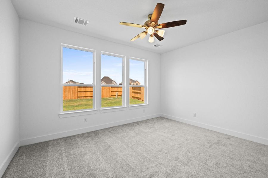As you enter the primary bedroom, you’re greeted by an abundance of natural light pouring in through large, beautifully framed windows, casting a warm glow on the soft, neutral tones of the walls.