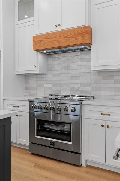 Kitchen with stainless steel range, light hardwood / wood-style flooring, backsplash, and white cabinetry