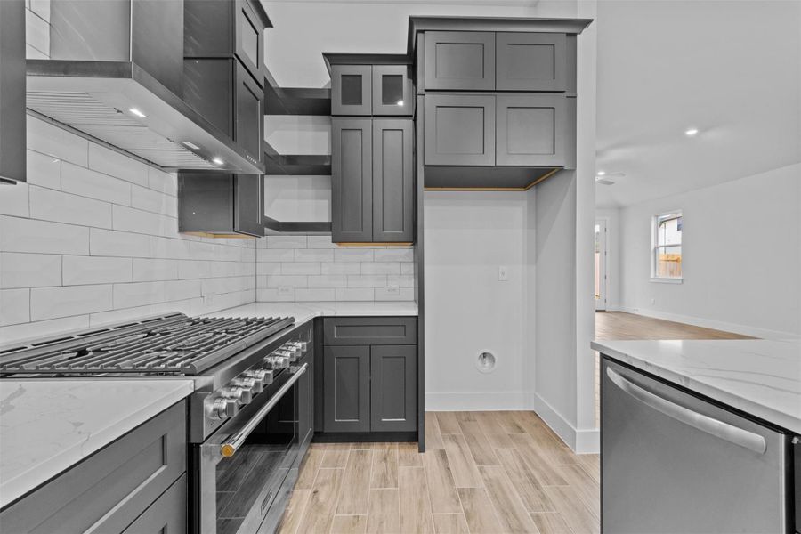 Kitchen with light stone countertops, backsplash, stainless steel appliances, and wall chimney exhaust hood