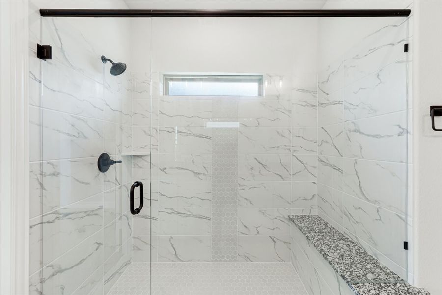 Walk-in shower with marble-look tile walls, glass door, built-in bench, and small window