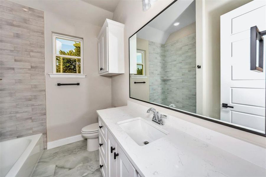 Full bathroom with vanity, tile patterned flooring, tiled shower / bath combo, and toilet