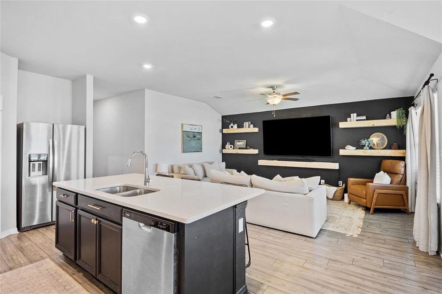 Kitchen with appliances with stainless steel finishes, an accent wall, a kitchen island with sink, vaulted ceiling, and light stone countertops