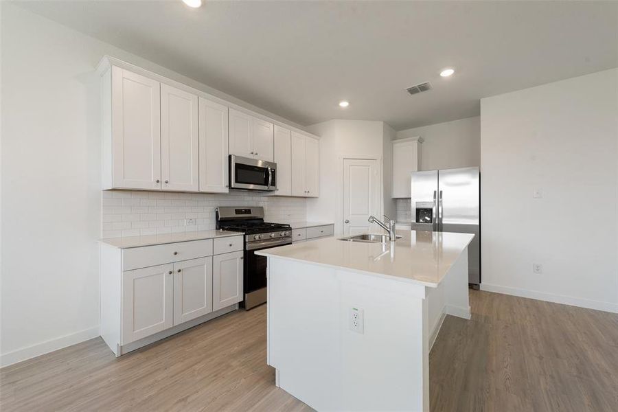 Kitchen featuring appliances with stainless steel finishes, light hardwood / wood-style floors, an island with sink, and white cabinets