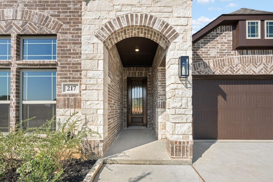 Home entrance with stone arch, dark iron front door, brick exterior, and attached garage