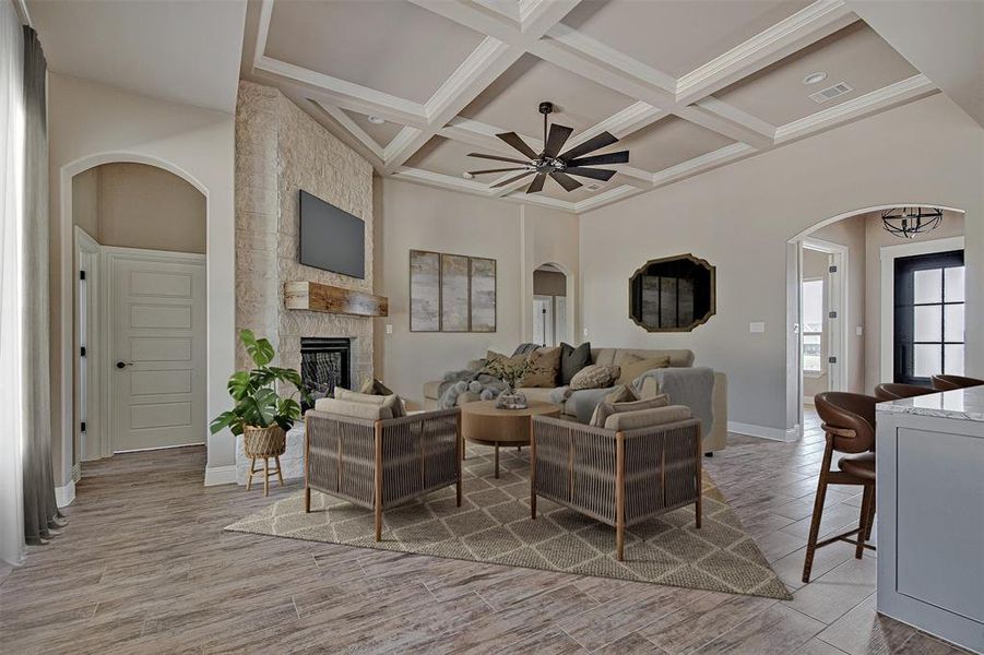 Living room with a stone fireplace, coffered ceiling, a towering ceiling, ceiling fan, and beam ceiling