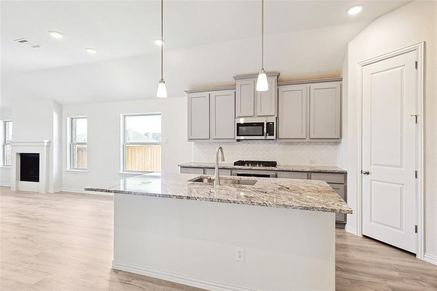 Kitchen with light wood-type flooring, light stone counters, a kitchen island with sink, sink, and gray cabinetry