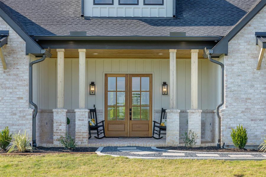 View of exterior entry featuring a porch, a shingled roof, french doors, and board and batten siding