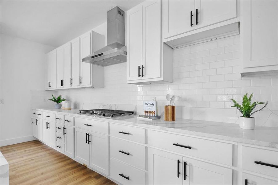 Kitchen featuring white cabinets, stainless steel gas stovetop, and wall chimney range hood