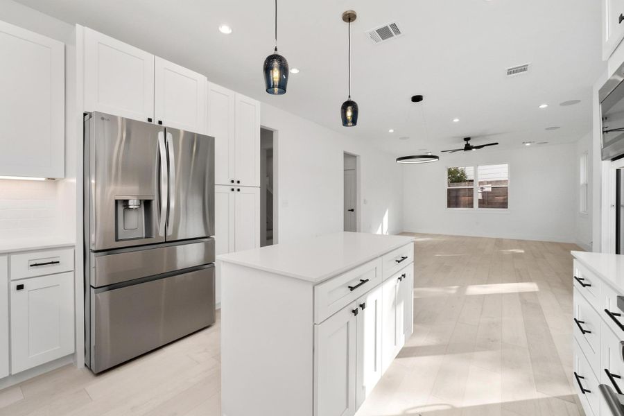 Kitchen featuring stainless steel fridge, a kitchen island, white cabinetry, and pendant lighting