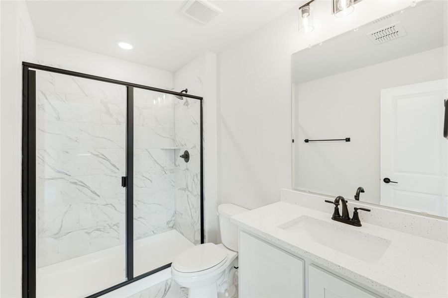 Bathroom with marble-tile shower, black glass door, white quartz vanity, and black fixtures