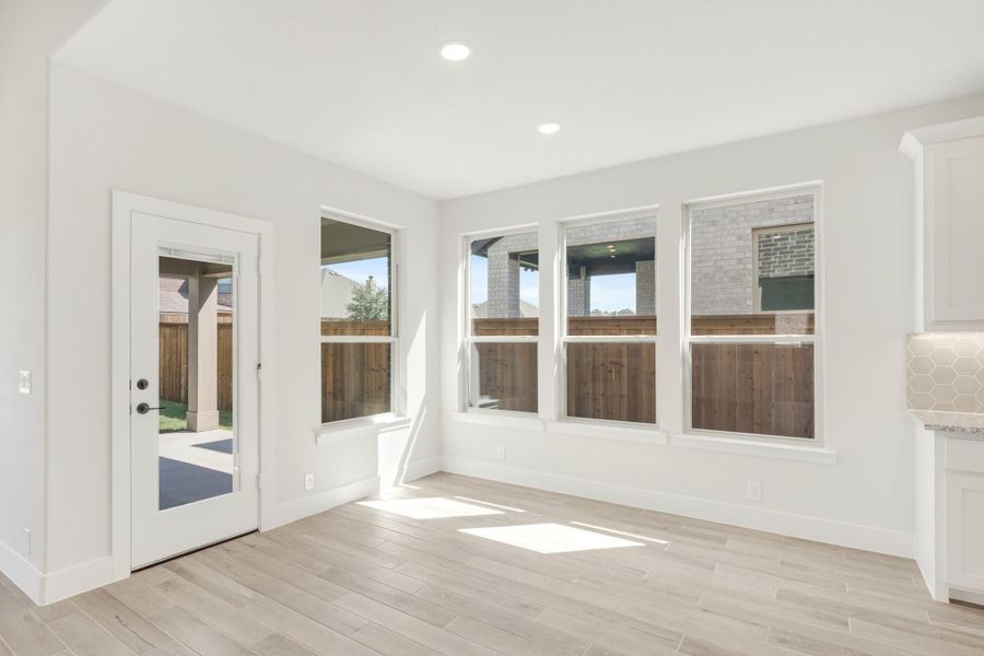 Bright dining area with light wood floors, four large windows, and glass back door leading to backyard