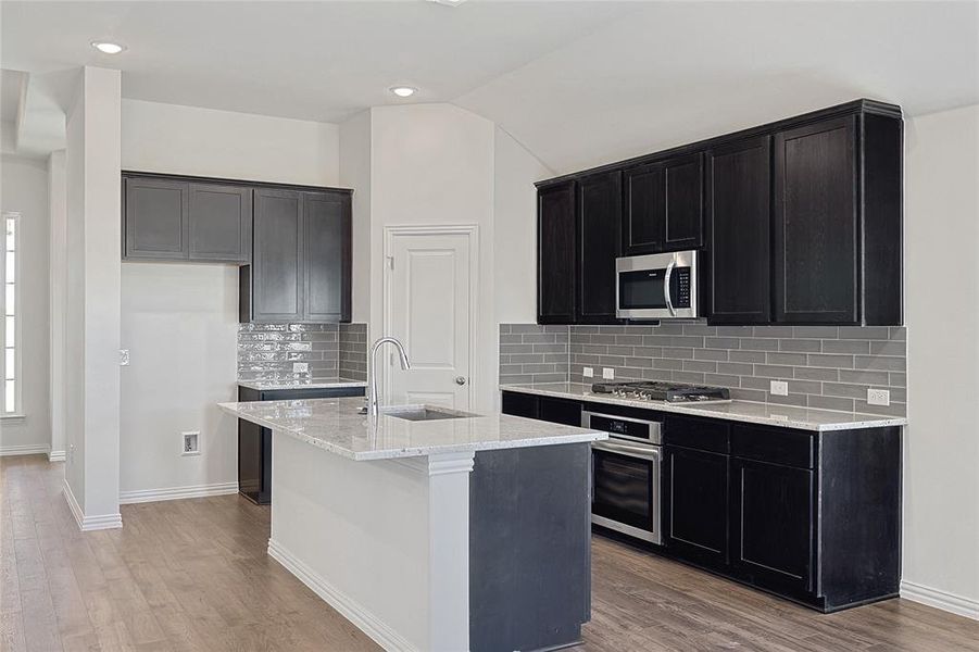 Kitchen featuring tasteful backsplash, an island with sink, light hardwood / wood-style floors, lofted ceiling, and appliances with stainless steel finishes