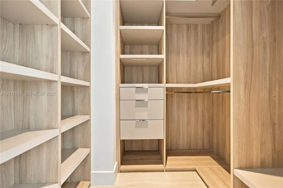 Custom walk-in closet featuring wood-finish cabinetry, built-in shelving, integrated drawers with metal pulls, and polished metal hanging rods Custom walk-in closet featuring wood-finish cabinetry, built-in shelving, integrated drawers with metal pulls, and polished metal hanging rods
