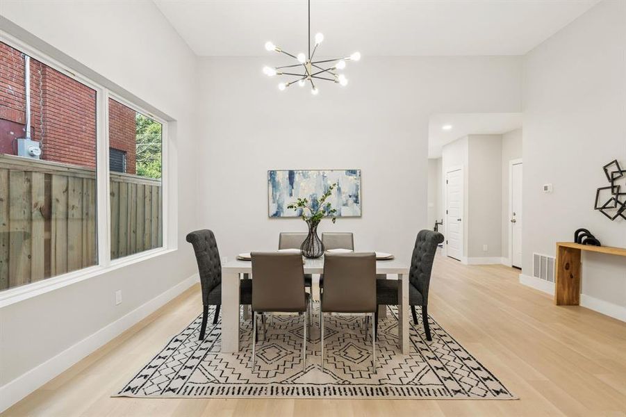 Spacious dining area featuring high vaulted ceilings, light wood-finish flooring, and a contemporary linear chandelier Spacious dining area featuring high vaulted ceilings, light wood-finish flooring, and a contemporary linear chandelier