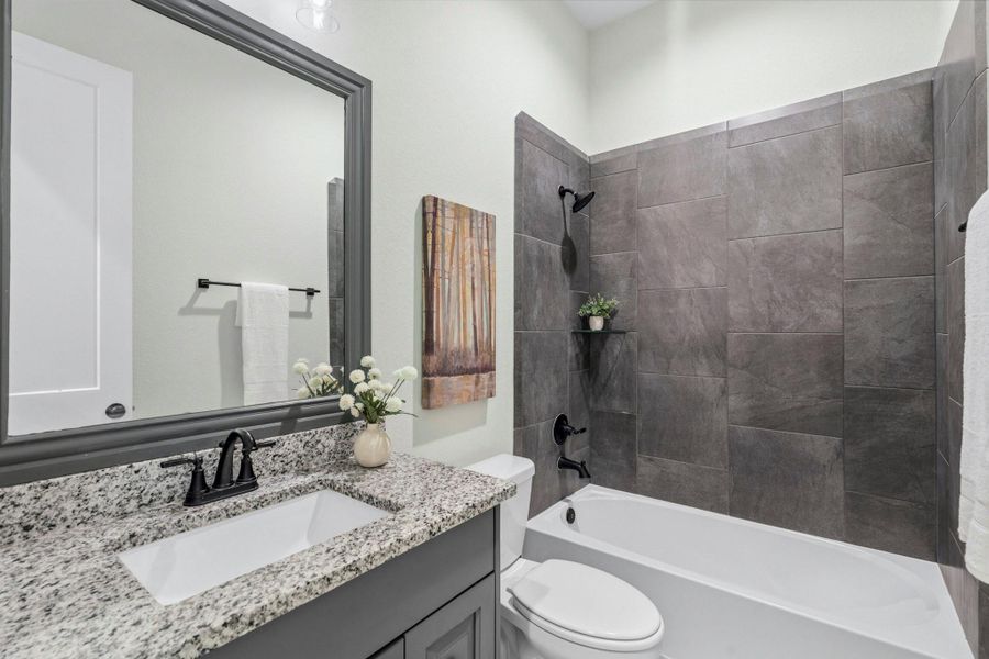 Two Secondary Bedrooms share this beautifully appointed central Full Bath, featuring an undermount sink, elegant granite countertops, and a framed mirror that adds a touch of sophistication. The shower/tub combination is enhanced by a dramatic, moody tile surround, creating a stylish space that blends everyday functionality with elevated design.