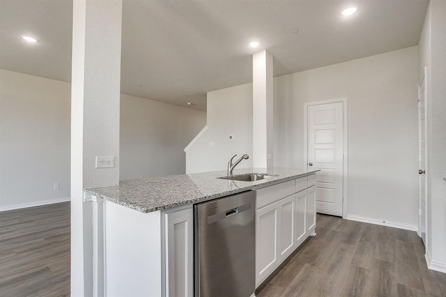 Kitchen with stainless steel dishwasher, light stone countertops, white cabinets, dark wood-style flooring, and recessed lighting
