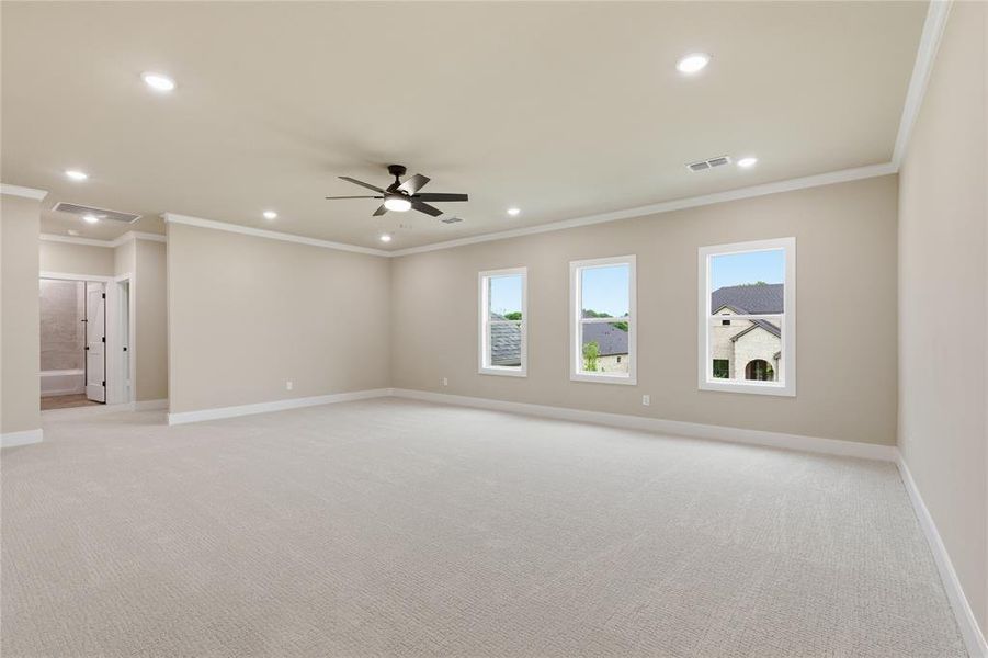 Spacious carpeted room featuring a ceiling fan, recessed lighting, crown molding, and three large windows Spacious carpeted room featuring a ceiling fan, recessed lighting, crown molding, and three large windows