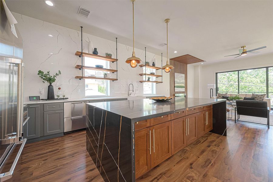 This is a modern, open-concept kitchen with stainless steel appliances, sleek gray countertops, and warm wooden cabinetry. The space features stylish pendant lighting and opens into a cozy living area with ample natural light. This is a modern, open-concept kitchen with stainless steel appliances, sleek gray countertops, and warm wooden cabinetry. The space features stylish pendant lighting and opens into a cozy living area with ample natural light.