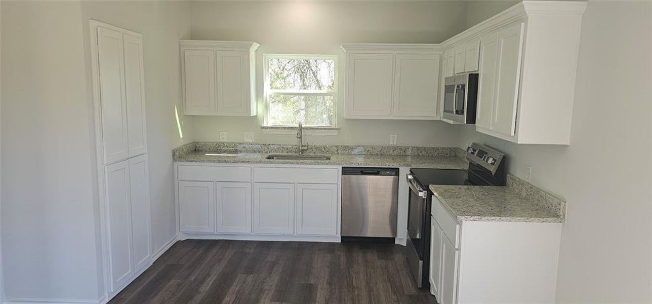Kitchen featuring white cabinets, appliances with stainless steel finishes, light stone countertops, and dark wood-style floors