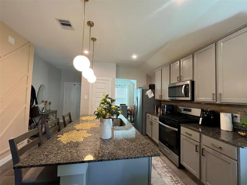 This modern kitchen features sleek gray cabinets, stainless steel appliances, and a granite countertop island with seating. Pendant lighting adds elegance, and the space is well-lit with natural light. Perfect for entertaining and daily living.