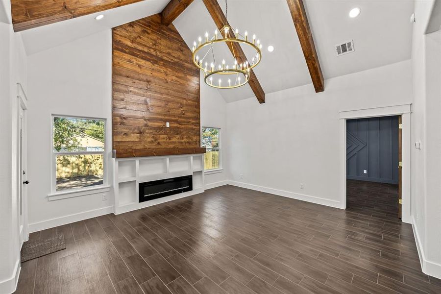 Unfurnished living room with high vaulted ceiling, beamed ceiling, wood finish floors, plenty of natural light, and a glass covered fireplace Unfurnished living room with high vaulted ceiling, beamed ceiling, wood finish floors, plenty of natural light, and a glass covered fireplace