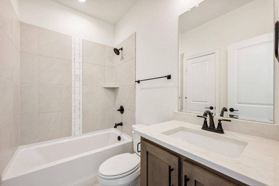 Bathroom with white tile tub-shower combo, single vanity with dark fixtures, and toilet