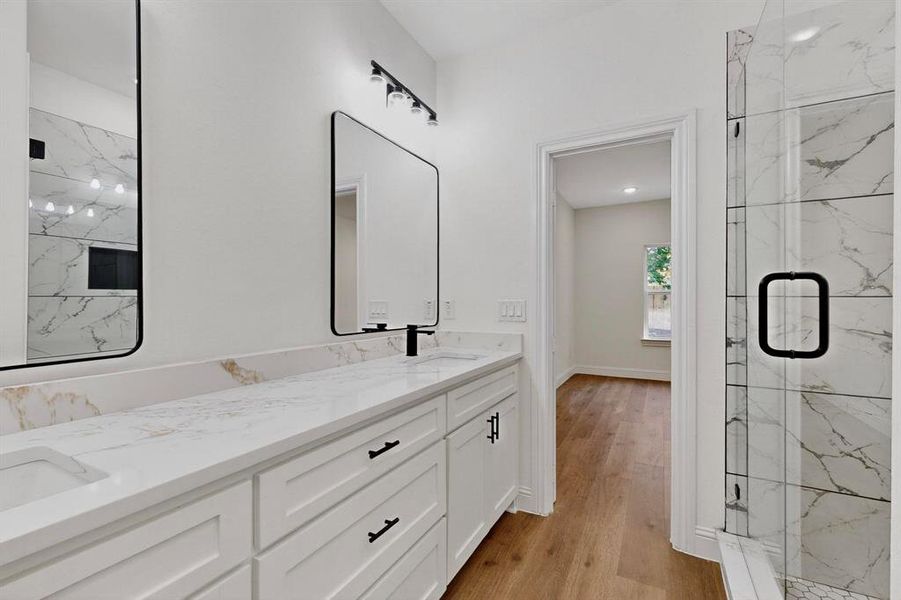 Full bathroom with a marble finish shower, light wood-style flooring, and double vanity