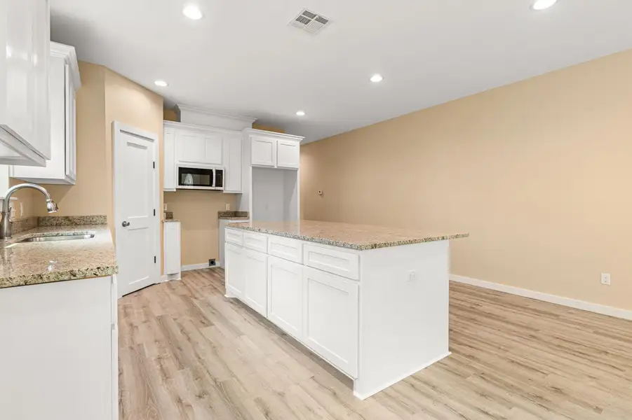 Kitchen featuring light wood-style floors, a center island, recessed lighting, white cabinets, and light stone counters