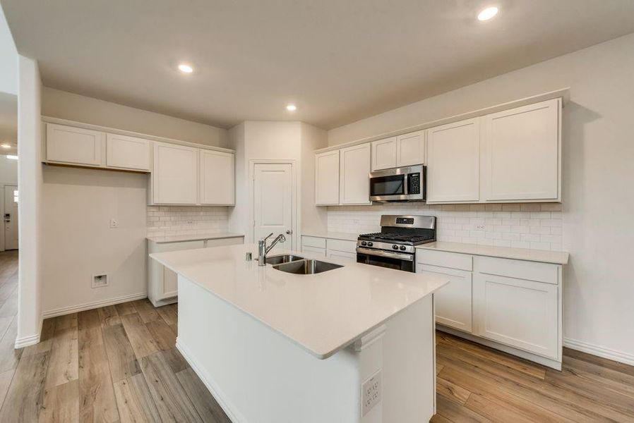 Kitchen featuring appliances with stainless steel finishes, white cabinetry, sink, an island with sink, and tasteful backsplash