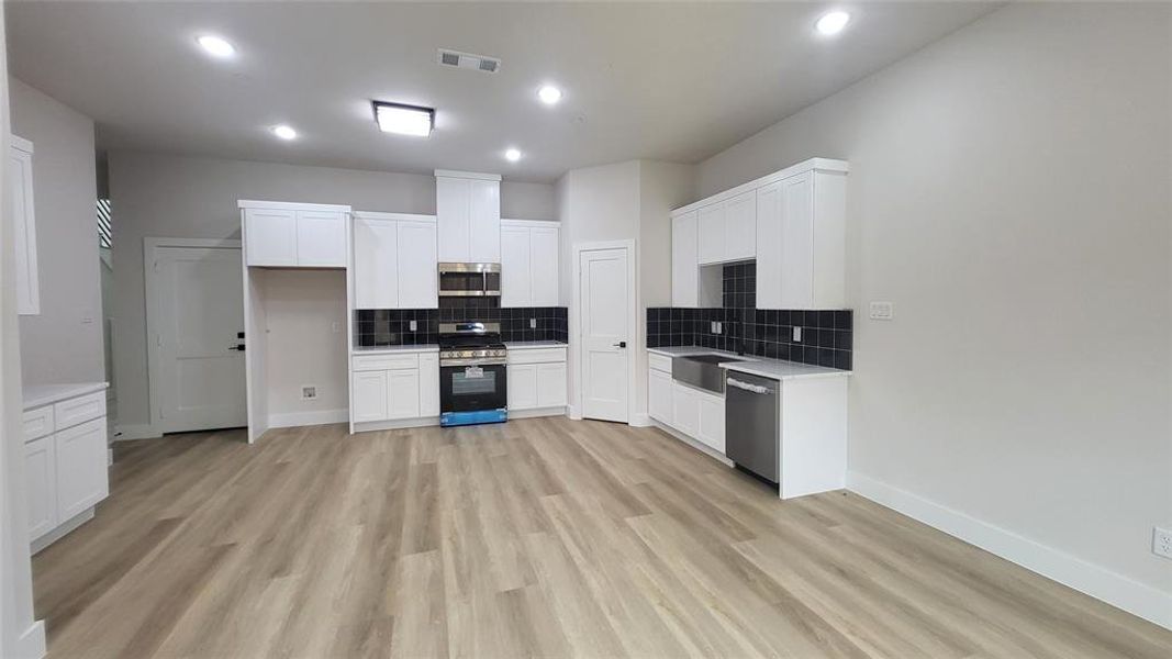 Kitchen featuring stainless steel appliances, visible vents, light wood-style floors, tasteful backsplash, and white cabinetry