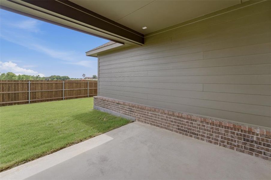 Covered patio area with a concrete slab, wood-finish siding, a brick base, and a fenced backyard with a manicured lawn