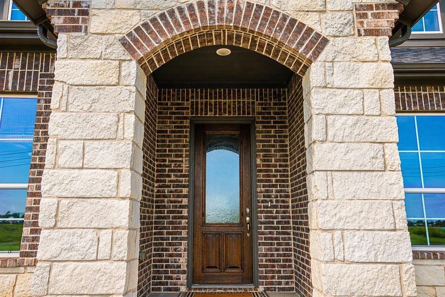 Front entry featuring a wood-panel door with an arched glass insert, set within a brick and stone facade
