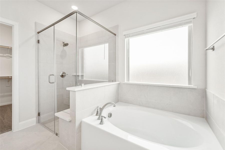 Master bathroom with soaking tub, glass-enclosed shower, and gray tile walls next to a walk-in closet