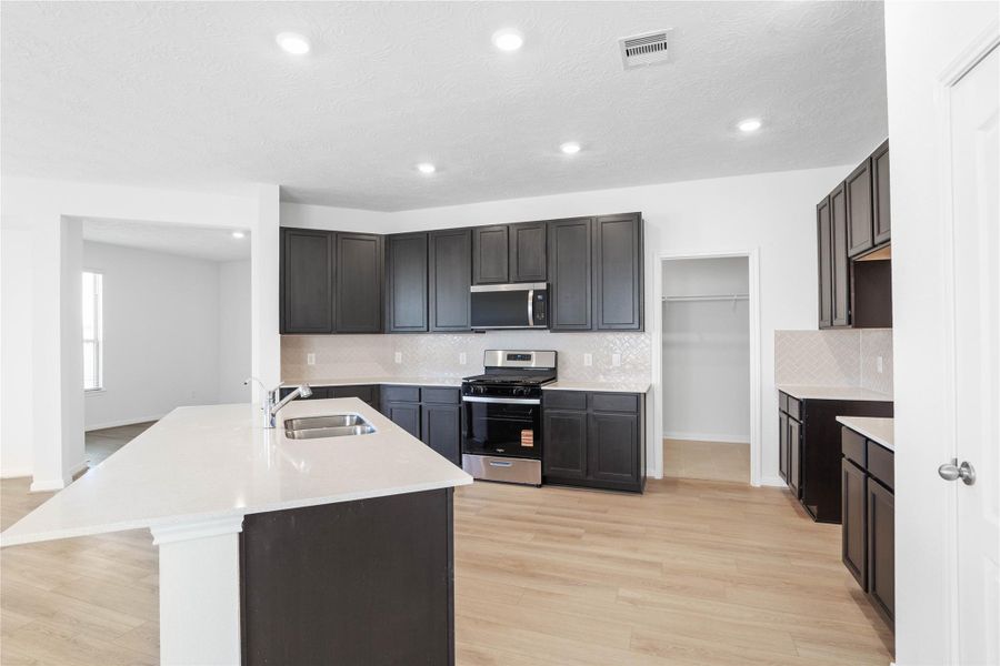 This spacious kitchen boasts high ceilings, Woodmont Belmont cabinets in an Espresso stain, Silestone Blanco Maple countertops, stainless steel Whirlpool appliances, a modern Daltile backsplash, recessed lighting, an extended breakfast bar countertop, and a pantry—all overlooking the expansive Great Room. This spacious kitchen boasts high ceilings, Woodmont Belmont cabinets in an Espresso stain, Silestone Blanco Maple countertops, stainless steel Whirlpool appliances, a modern Daltile backsplash, recessed lighting, an extended breakfast bar countertop, and a pantry—all overlooking the expansive Great Room.