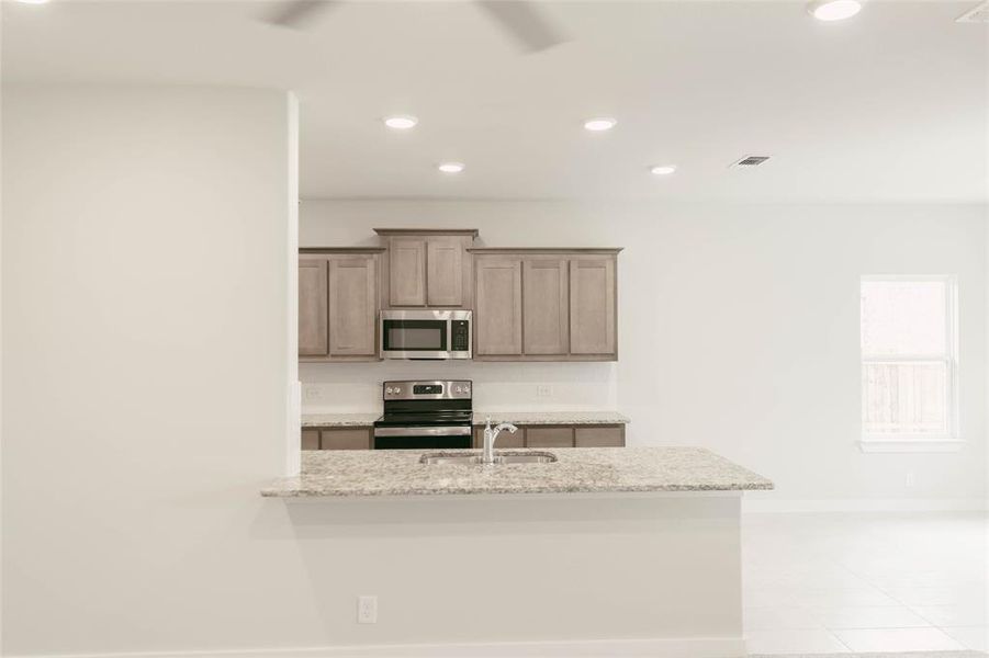 Kitchen with sink, light tile patterned flooring, light stone counters, and stainless steel appliances