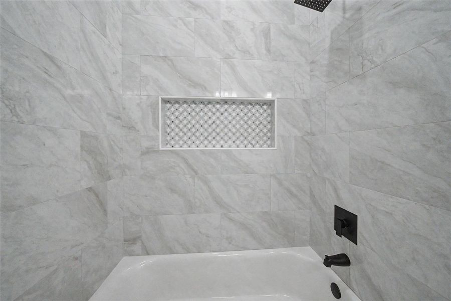 Stylish secondary bath detail with floor-to-ceiling tile and a decorative shower niche.