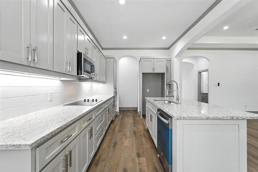 Kitchen featuring dark wood-style floors, light stone counters, tasteful backsplash, a kitchen island with sink, and stainless steel appliances Kitchen featuring dark wood-style floors, light stone counters, tasteful backsplash, a kitchen island with sink, and stainless steel appliances