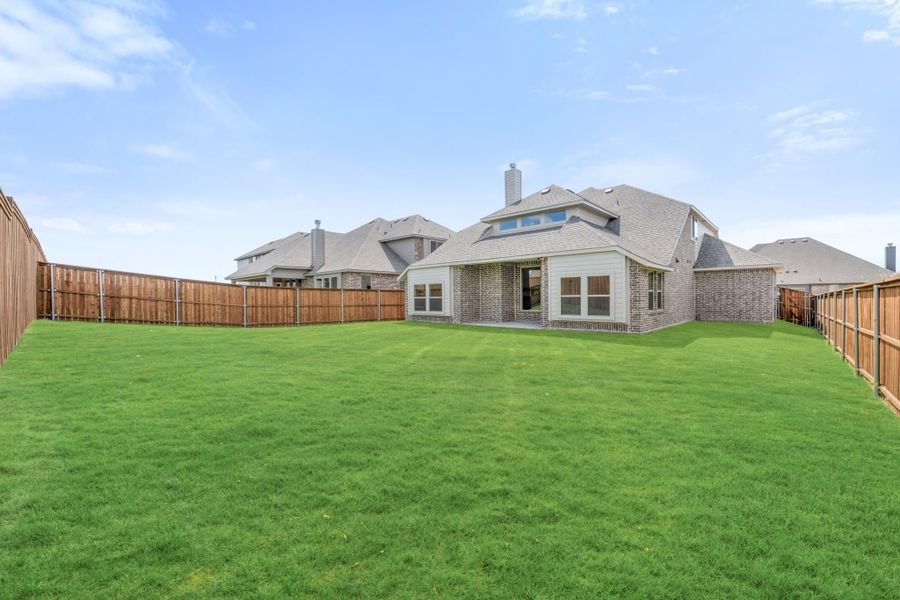 Brick home rear view with large grassy backyard enclosed by wood privacy fence