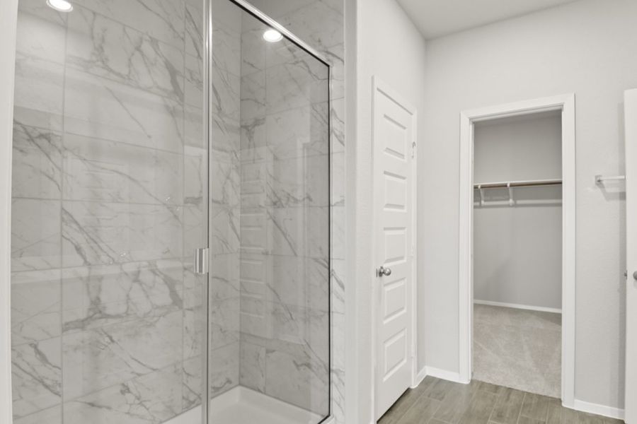 Image of a primary bathroom with a standing walk-in shower and marble-like tile with a connecting walk-in closet Image of a primary bathroom with a standing walk-in shower and marble-like tile with a connecting walk-in closet