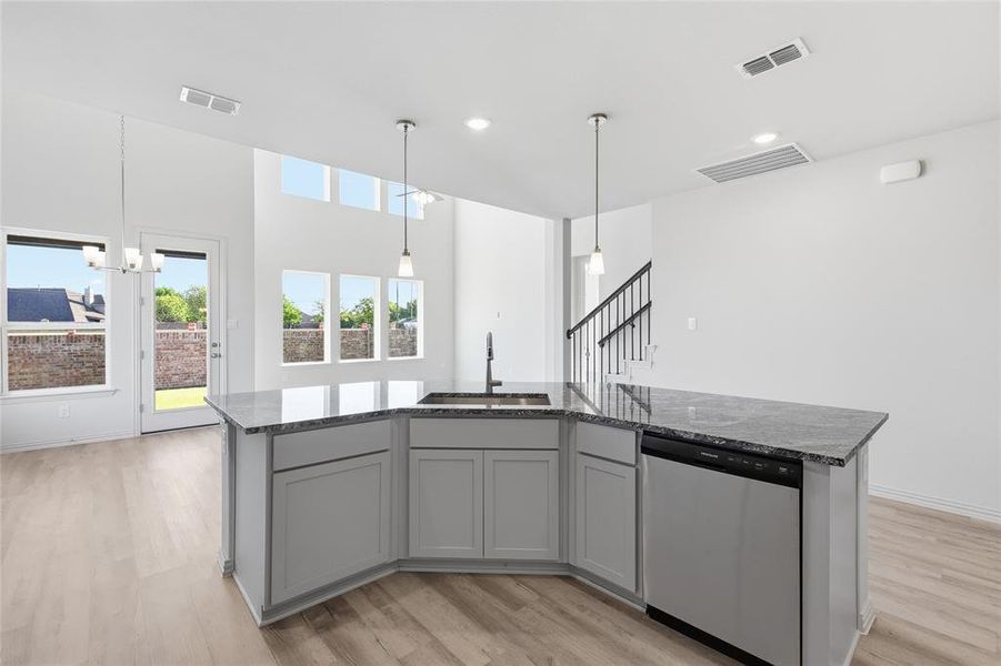 Kitchen with an island with sink, dishwasher, gray cabinetry, light wood-style floors, and pendant lighting Kitchen with an island with sink, dishwasher, gray cabinetry, light wood-style floors, and pendant lighting