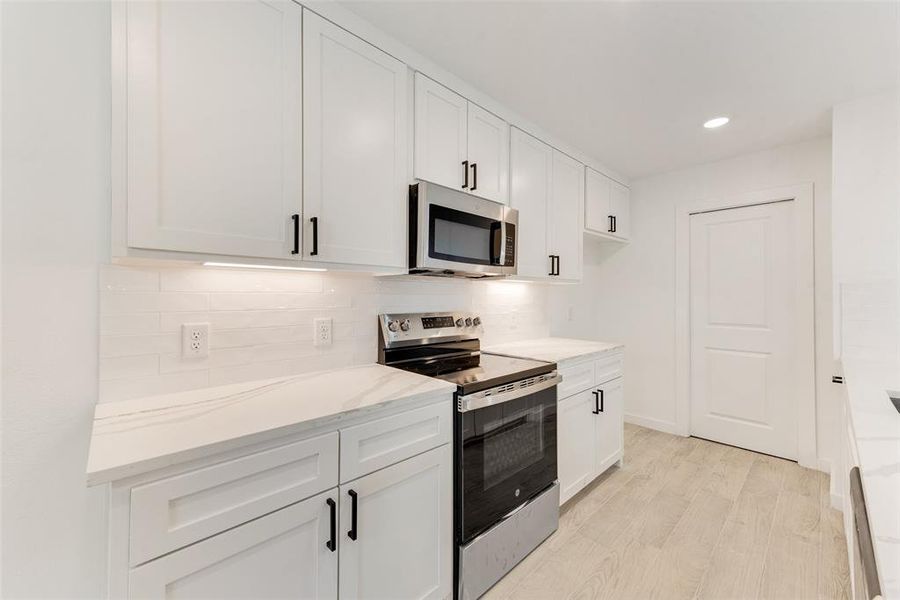 Kitchen featuring tasteful backsplash, white cabinetry, light hardwood / wood-style floors, stainless steel appliances, and light stone countertops