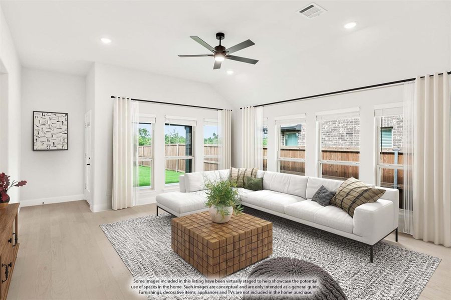 Bright living room with vaulted ceiling, ceiling fan, white sectional sofa, and large windows overlooking backyard